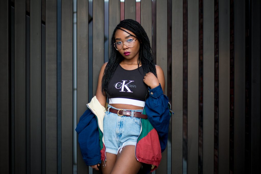 jeune femme portant un look vintage avec un short en jean taille haute un crop top calvin klein une veste de survêtement colorée